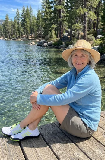 Older woman sitting by a mountain lake wearing Grounded Footwear barefoot shoes